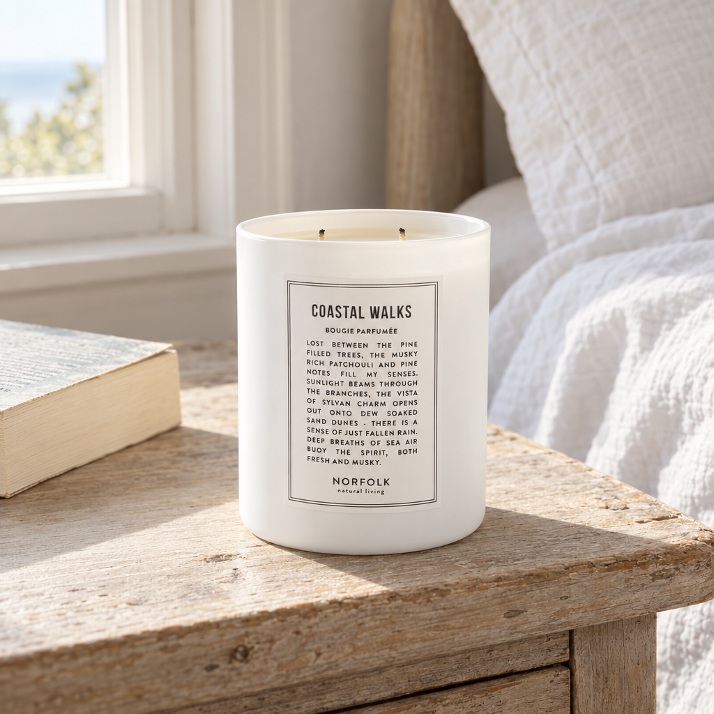 Norfolk Natural Living Coastal Walks two-wick candle on an oak bedside table in a coastal cottage bedroom