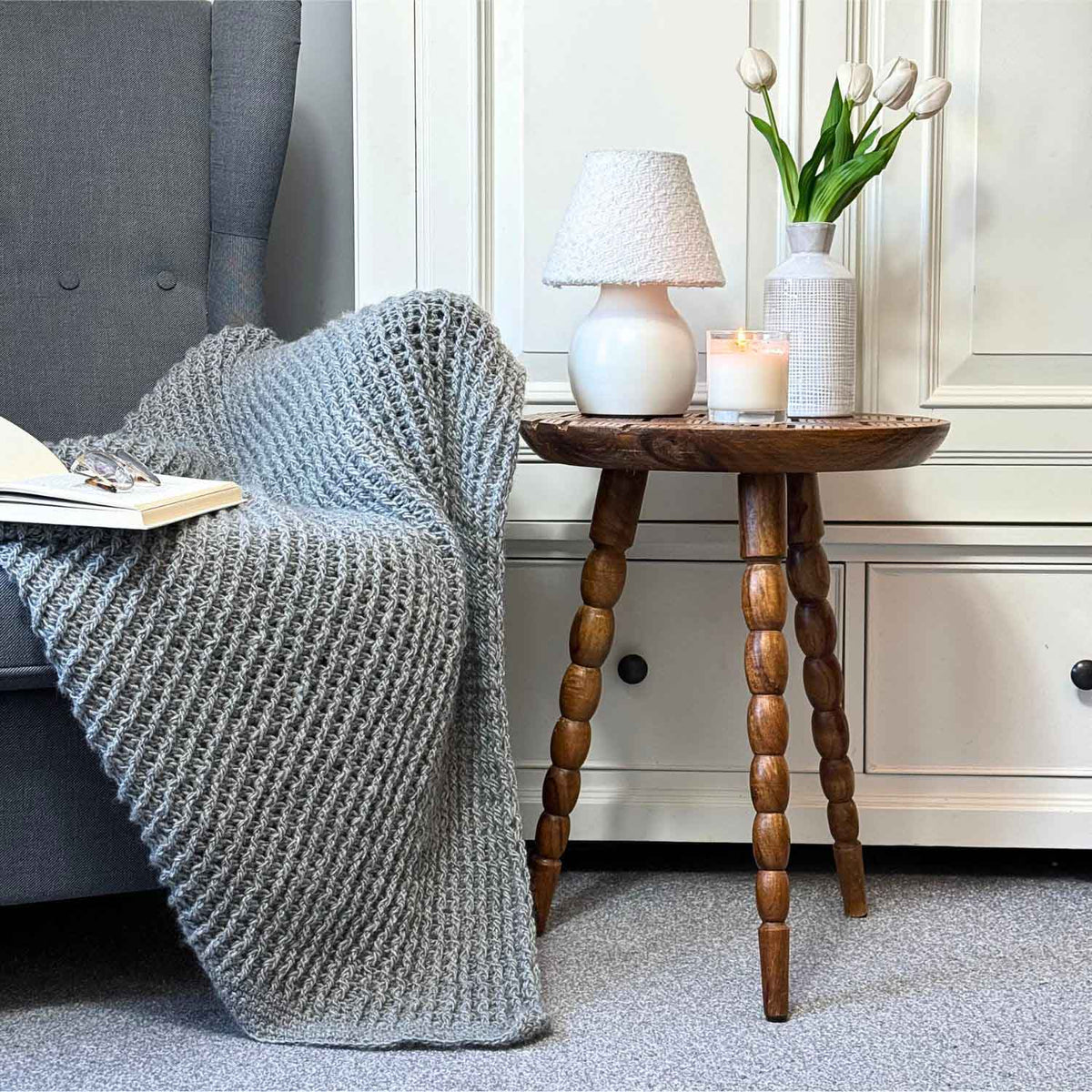 A handsome, small wooden side table, placed next to a soft, grey arm chair for stylish quiet luxury living|||