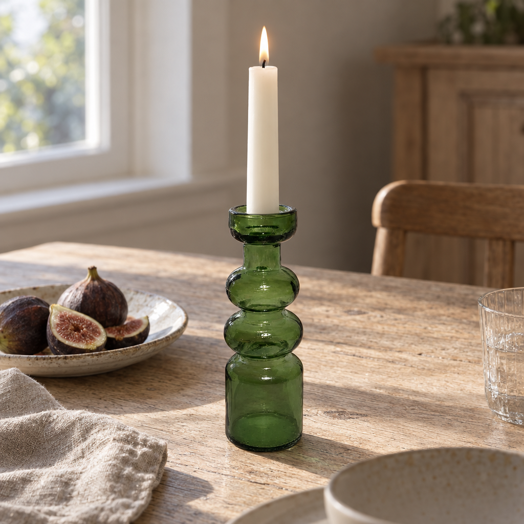 Moss green recycled glass candlestick with a lit candle on an oak table