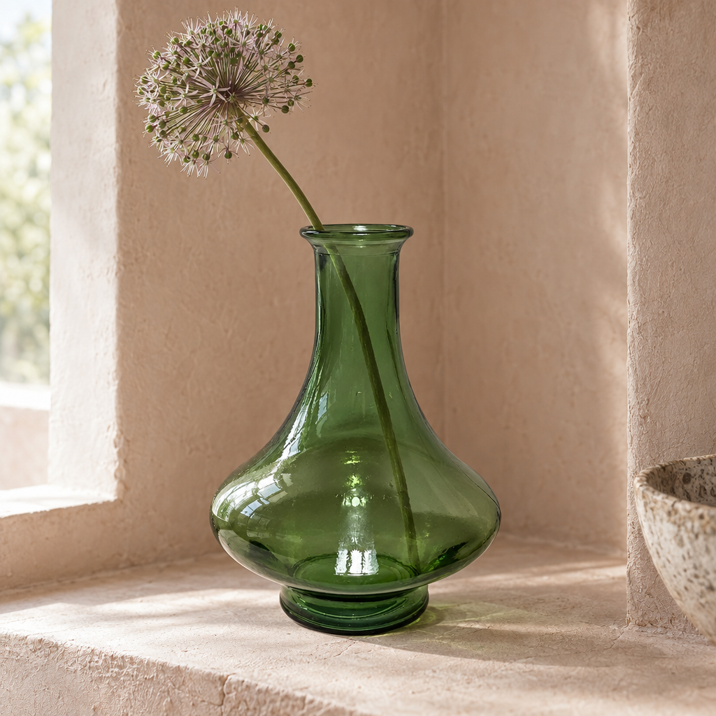 Green recycled glass tajine vase with an allium stem in a plaster alcove